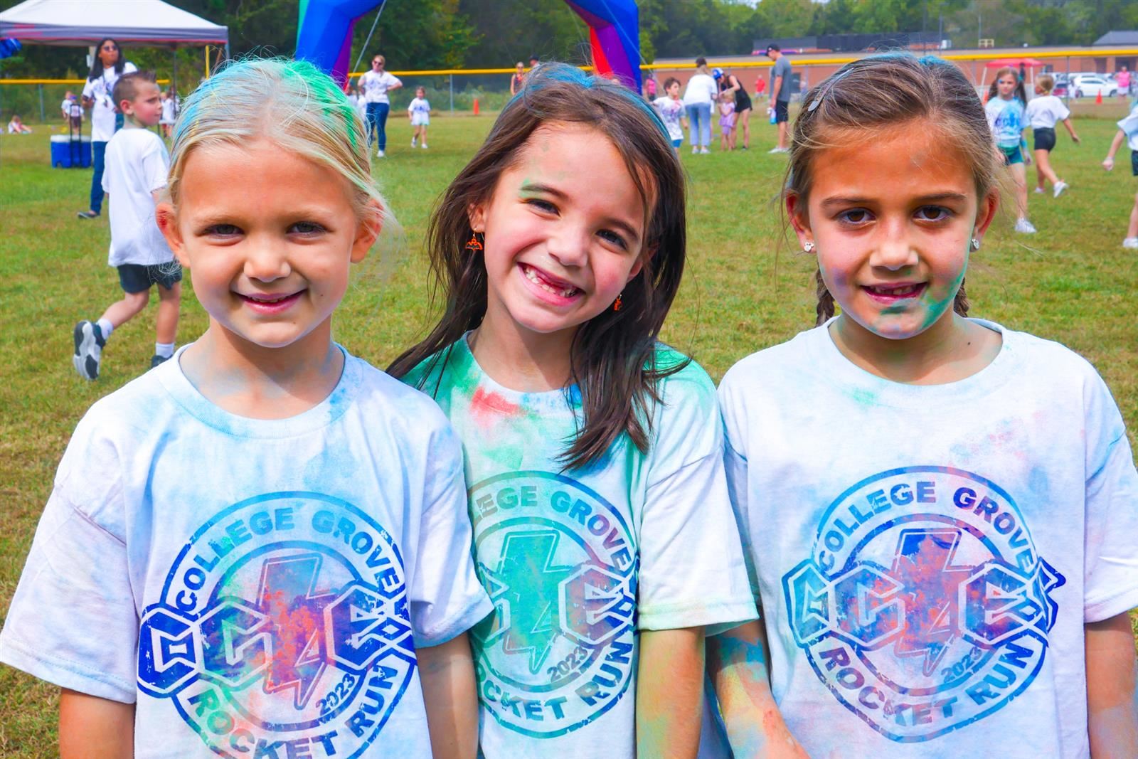 three girls smiling with colored powder on their shirts and hair